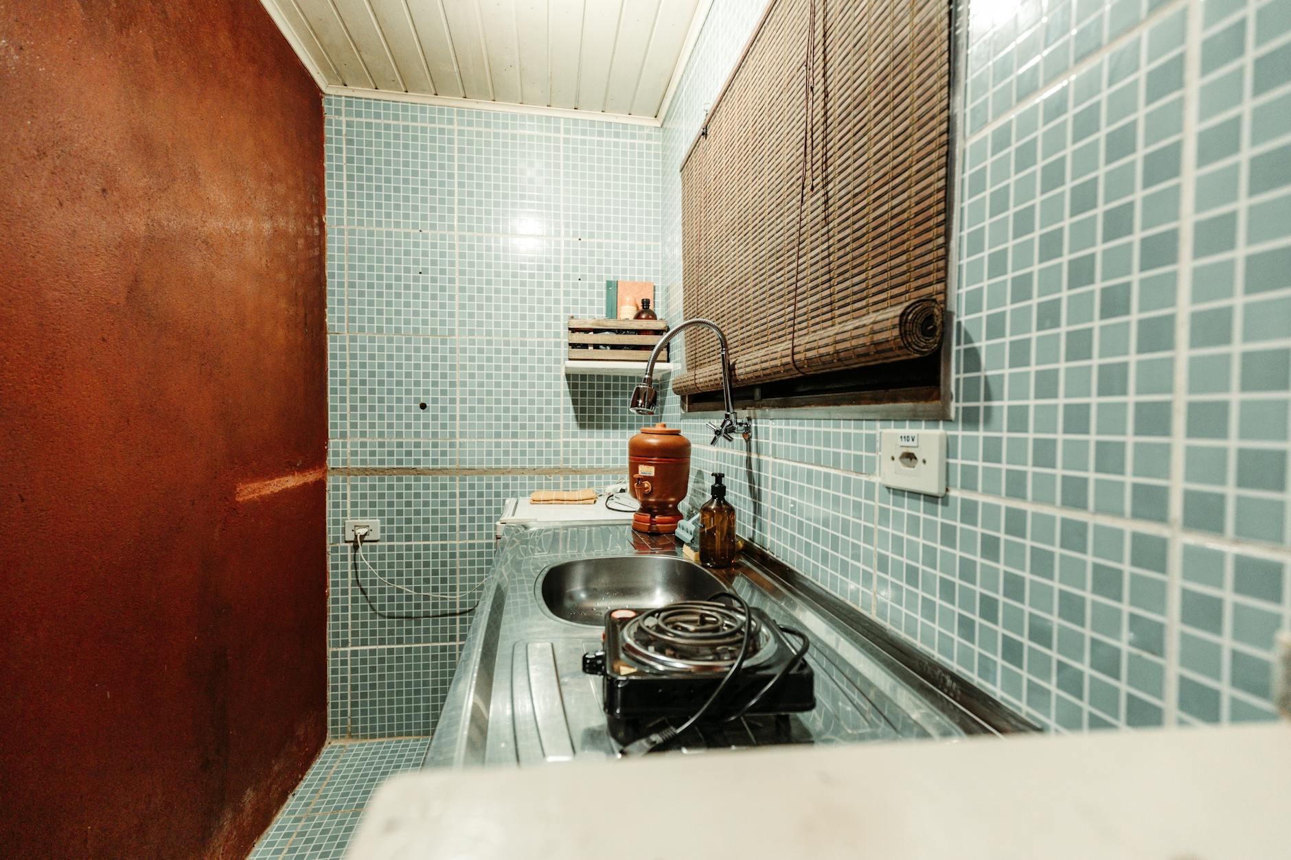 Mały aneks kuchenny z niebieskimi płytkami, zlewem i jedną płytą elektryczną