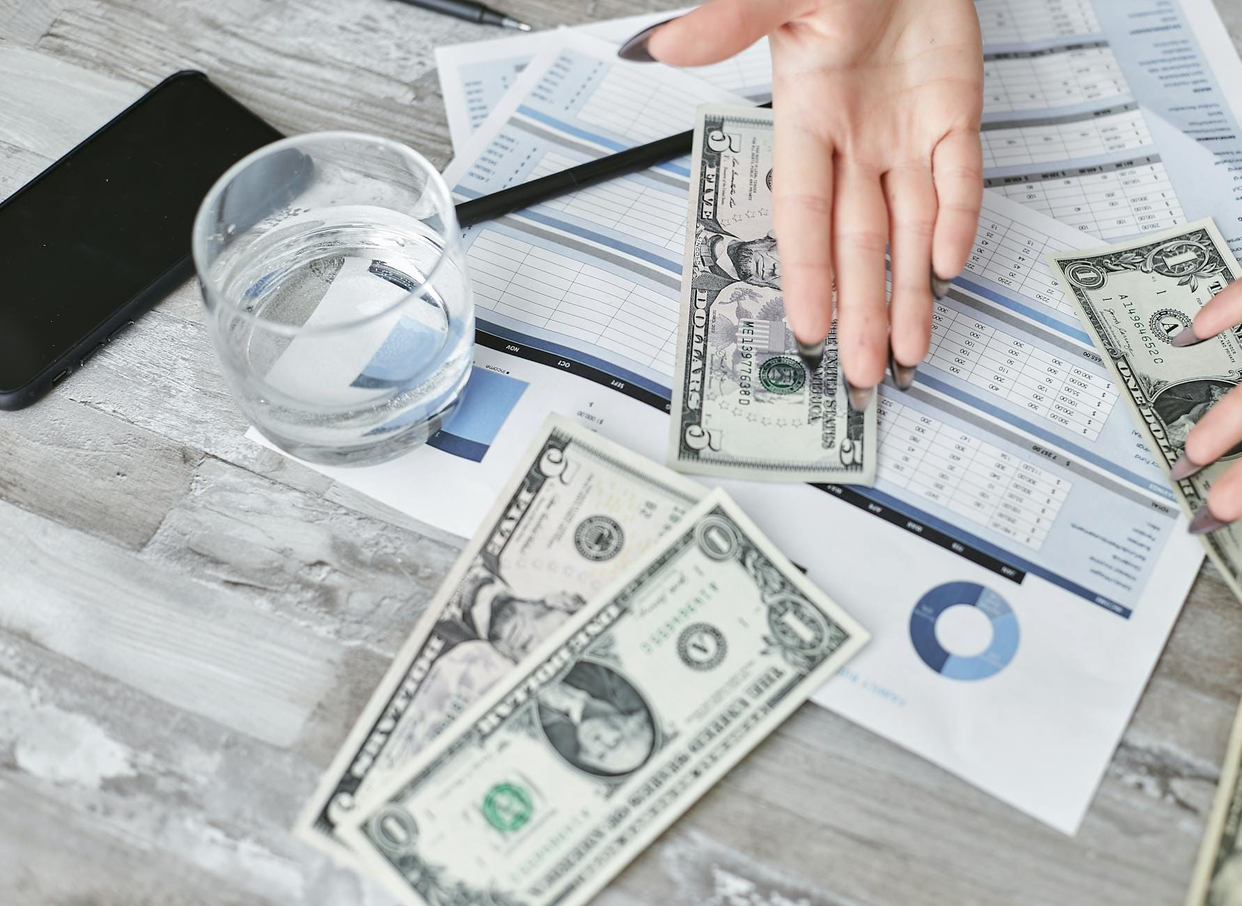Dokumenty finansowe z banknotami dolarowymi i szklanką wody na biurku