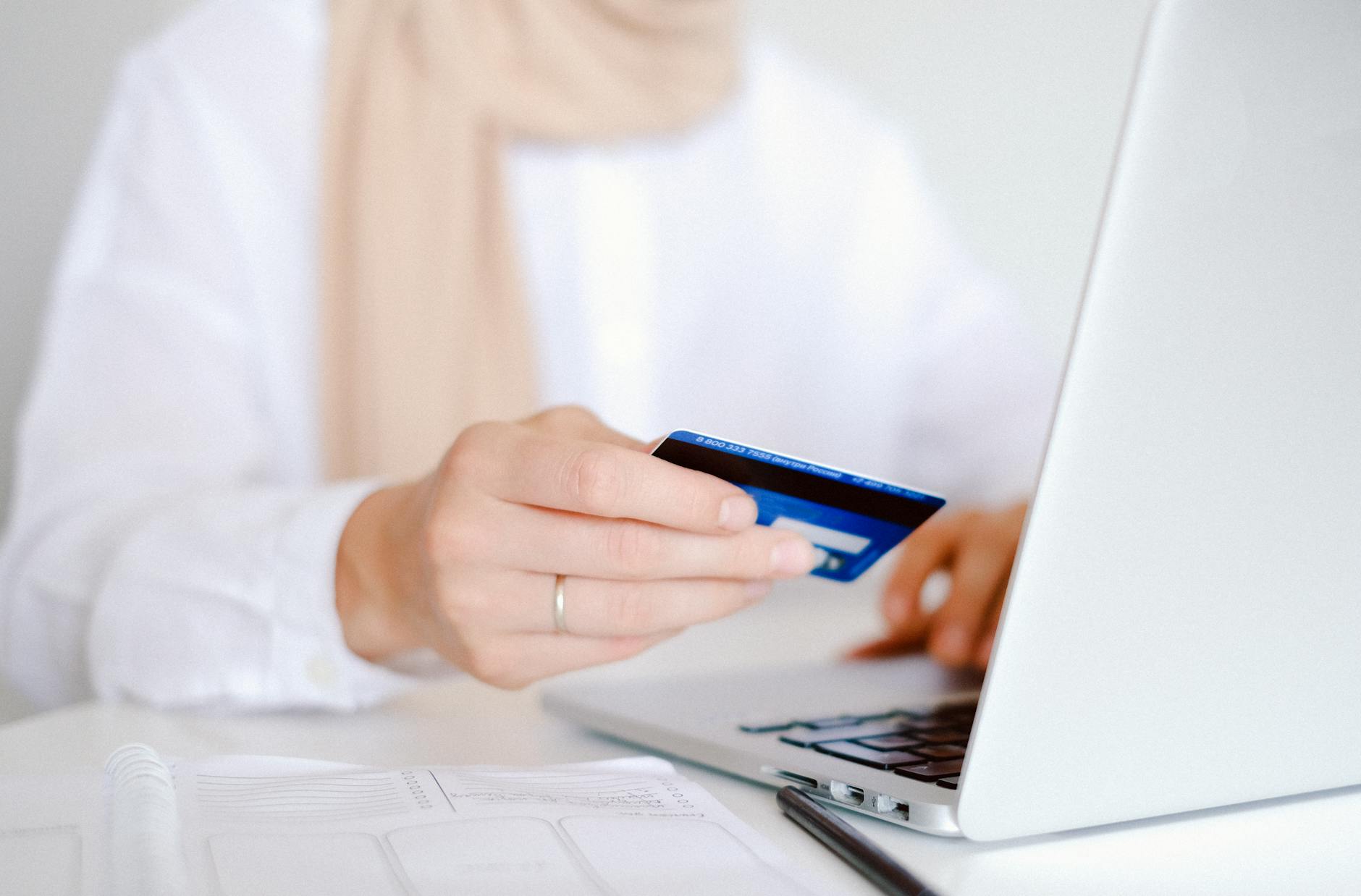 Osoba trzyma kartę płatniczą i robi zakupy online na laptopie