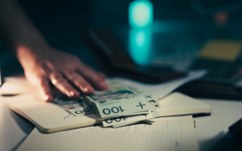 Dłoń sięgająca po banknoty na biurku z notesem i kalkulatorem
